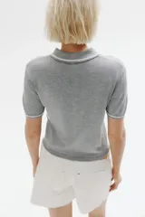Remera polo corta de punto fino color gris con cuello, tapeta de botones y mangas cortas con ribete blanco.