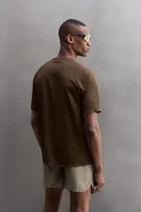 Camiseta deportiva marrón con estructura perforada, cuello redondo, manga corta y logo estampado.