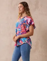 Blusa estampada con motivos florales en tonos rosa, azul y naranja. Tiene cuello en V y mangas cortas con volados.