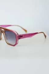Lentes de sol de mujer con armazón grueso de policarbonato color rosa translúcido y lentes oscuros degradados. Diseño de montura geométrica con puente doble.