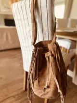 Cartera tipo bolso marrón de gamuza con flecos largos a los lados y correa de hombro fina.