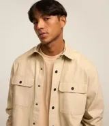 Camisa marrón de manga larga, confeccionada en sarga, con cuello inglés, abotonado delantero, bolsillos en el pecho con solapa y puños abotonados.