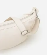 Bolso mediano color crema, con forma de media luna y correa ajustable con aros metálicos.
