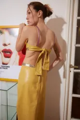 Vestido midi de cuero color maíz con cortes laterales y detalles dorados. Tiene tiras finas fucsias y abertura lateral en la falda.