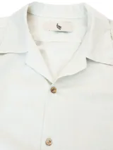 Camisa de manga corta color crema, con cuello camp y calce relajado. Confeccionada en una mezcla de lino y algodón, con botones de madera y parche característico de Polonio.