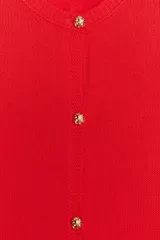Chaqueta roja de punto con cuello redondo y manga larga. Tiene bolsillos delanteros de plastrón, cierre frontal con botones dorados con relieve y acabados en rib.