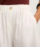 Short blanco de corte runner evasé, con cintura elástica fruncida y un botón decorativo. Presenta bolsillos laterales y un calce suelto.