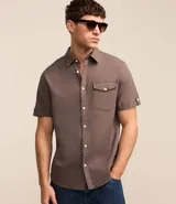 Camisa de hombre de manga corta en lino color blanco, con cuello clásico, botonadura frontal y bolsillo de parche en el pecho. Corte recto.