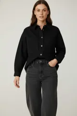 Sobrecamisa de denim negro, con cuello camisero, botones frontales y dos bolsillos de parche con tapa en el pecho. Presenta un calce holgado y mangas largas.