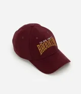 Gorra de sarga color borgoña con bordado frontal de la palabra "Brooklyn" en color dorado.