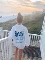 Hoodie blanco con estampado en la espalda que dice "Glassy Waves", "Good Vibes", una flor celeste, "Enjoy the beach and the sun" y los años "1971, 1982, 1999".