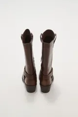 Bota de caña media color negro, estilo motociclista o cowboy, con puntera cuadrada y taco bajo. Presenta una tira ancha con hebillas metálicas alrededor del tobillo.