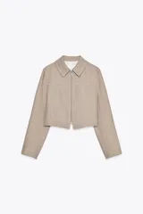 Chaqueta corta color beige con cuello solapa, manga larga y cierre frontal con cremallera.