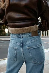 Pantalón de jean azul de tiro alto, corte mom fit, tobillero y con cinco bolsillos. Cierre frontal con cremallera y botón.