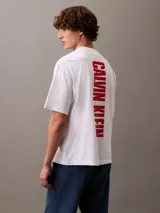 Remera blanca de algodón con cuello redondo, mangas cortas y logo de Calvin Klein Jeans estampado verticalmente en color rojo en el pecho.