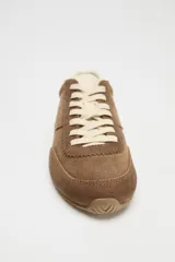 Zapatillas deportivas color marrón de piel con detalle de pespuntes, suela dentada, forro interior y parte trasera en contraste color crema. Cierre con cordones y acabado en punta redonda.