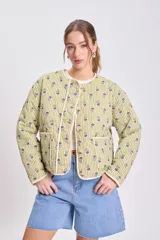 Chaqueta acolchada color verde claro con rayas verticales y pequeños estampados florales en tonos azules y verdes. Tiene cuello redondo, cierre frontal con botones y ribetes de color crudo.