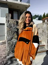 Buzo de terciopelo color tostado, beige y negro, con cierre de media cremallera, cuello alto con botones a presión y bolsillo tipo canguro con solapa y botón.