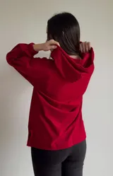 Canguro rojo de corte oversize con pinzas en las mangas, tajo a los lados y bolsillo tipo canguro. Tiene cuello con cordones ajustables.