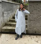 Camisa vestido larga a rayas verticales celestes y blancas, con cuello camisero, cierre frontal con botones y mangas largas.