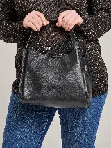 Bolso tipo tote de cuero sintético negro con doble asa corta y cierre superior con botón imantado.