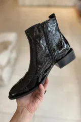 Bota corta de cuero vacuno color negro charol, con elástico lateral, punta fina y detalles de calado.