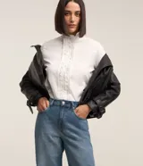 Camisa blanca de tricolina con cuello padre, abotonada al frente con detalle ondulado y mangas largas.