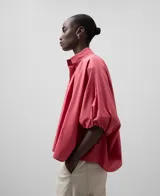 Camisa amplia de algodón color rosa, con cuello mao fruncido y bordado a tono. Manga corta con puño fruncido, botonadura frontal oculta con bordado a tono, bajo asimétrico y pliegue en la espalda.