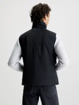 Chaleco negro acolchado de nailon reciclado con cuello alto, cierre de cremallera, bolsillos con cremallera en la cintura y logo de Calvin Klein en el pecho y la nuca.