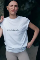 Remera deportiva blanca de corte holgado con cuello redondo ribeteado acanalado y bajo recto. Estampado frontal con la frase "In My Sculpting Era" en color negro.