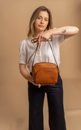 Bandolera color marrón de cuero sintético, con correa larga regulable, cierre superior y bolsillo frontal con cierre.