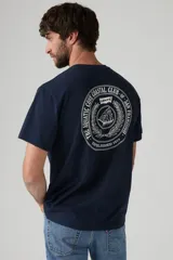 Remera azul marino de corte recto y mangas cortas, con cuello redondo y estampado en el pecho con un logo de un velero dentro de una corona de laureles.