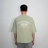 Remera verde con estampado en el centro de la espalda que dice 'Secret Company' con un globo terráqueo y una frase en inglés. Corte oversize.