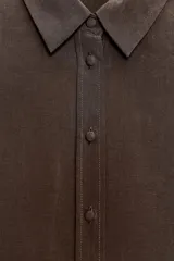 Camisa marrón de corte holgado, con cuello de solapa, manga larga con pliegues y bajo asimétrico. Cierre frontal con botones.