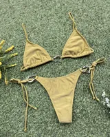 Conjunto de bikini color verde oliva (pistacho) compuesto por un corpiño triangular con argolla central y una bombacha colaless con tiras laterales ajustables y argollas laterales. Las argollas son de zamak.