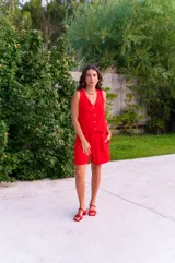 Conjunto de dos piezas color rojo vibrante, compuesto por un chaleco sin mangas con escote en V y botones frontales, y un short de tiro alto con pliegues y bolsillos laterales.