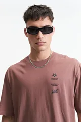 Remera marrón de manga corta con corte oversize y cuello redondo. Estampado en la espalda con diseño abstracto y texto.