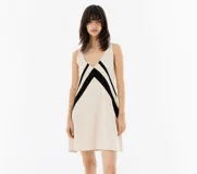 Vestido corto de tela liviana color crema, con escote en V y diseño de patchwork con piezas de tela negra que crean una V.
