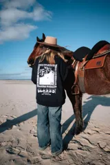 Buzo negro de corte holgado con estampa en la espalda con la leyenda 'Glassy Surfing 1999 Surf-Travel Club'.