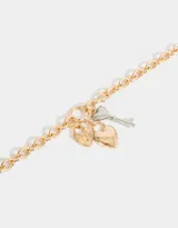 Collar corto dorado con cadena de eslabones gruesos y dijes colgantes: candado con forma de corazón, corazón liso y llave plateados.