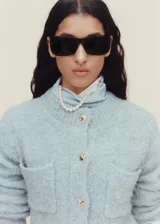 Chaqueta color celeste de tejido bouclé con cuello redondo, cierre frontal con botones efecto joya, dos bolsillos de parche frontales y mangas largas.