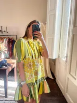 Vestido túnica corto con estampado de flores y rayas verticales en tonos amarillo, verde y marrón. Tiene cuello mao, mangas cortas abullonadas y volantes en el ruedo.