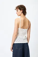 Top blanco de encaje con breteles finos, corte en la cintura y abertura frontal.