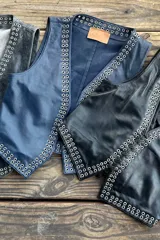 Chaleco negro de cuero con escote en V y cierre frontal con cordones. Presenta ojalillos metálicos plateados a lo largo de los bordes.