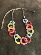 Collar con aros de acrílico entrelazados con tiento sintético color chocolate. Tiene nudo ajustable para regular el largo.