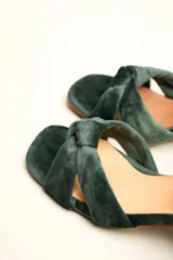Sandalia de terciopelo verde con taco cuadrado de 7 cm, punta cuadrada y tiras anchas anudadas en el empeine. Cuenta con una tira fina ajustable al tobillo con hebilla dorada.
