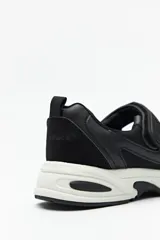 Zapatilla negra con tira ajustable y velcro.