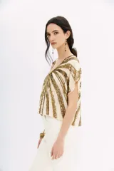 Blusa color crema con escote en V y mangas cortas tipo kimono. Presenta un diseño de rayas horizontales con lentejuelas doradas.