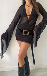 Minivestido negro de microtul transparente con corte irregular y mangas largas.