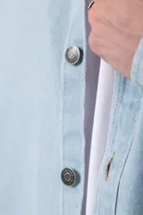 Chaqueta de jean celeste de corte recto, con cuello clásico, cierre frontal con botones metálicos y bolsillo de parche en el pecho.